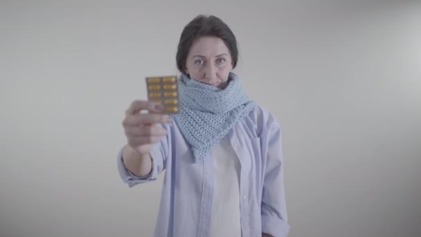 Portrait of adult Caucasian woman holding blurred blister pack of pills. Brunette lady showing medicine at camera standing on white background. Illness, treatment, therapy. — Stock Video