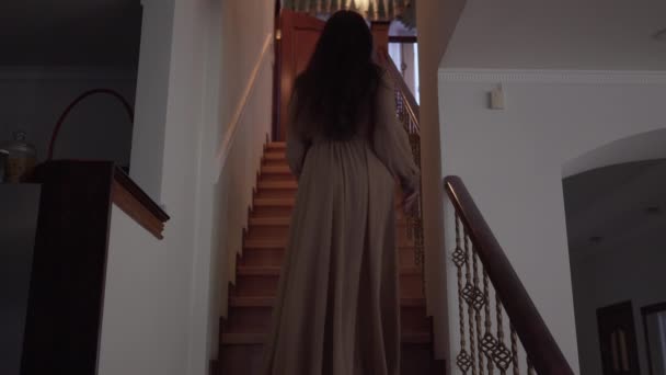 Zadní pohled na strašidelnou ženu, kráčející pomalu po schodech a vstupující do místnosti v domě. Bruneta bosá čarodějnice uvnitř. Magie, hrůza, noční můra, paranormální. — Stock video