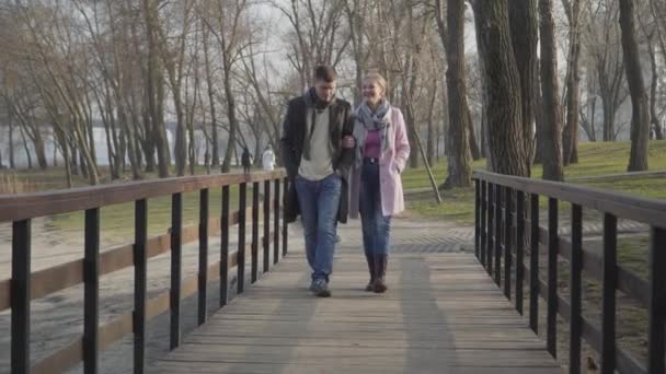 Amplio plano de hombre y mujer caucásicos relajados caminando por el callejón del parque en el soleado día de otoño. Felices amores marido y mujer paseando al aire libre los fines de semana. Relación, amor, romance, estilo de vida . — Vídeos de Stock