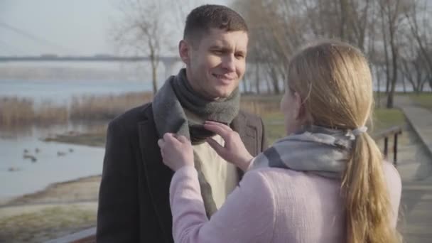 Primo piano di donna caucasica bionda irriconoscibile che ripara sciarpa uomo all'aperto. Felice giovane uomo che parla con il coniuge adorabile nel parco della città. Amore, affetto, stile di vita . — Video Stock