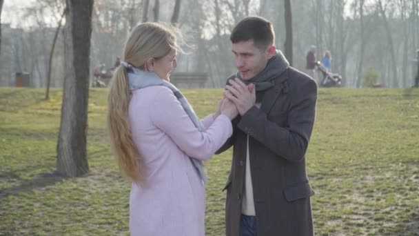 Retrato del joven hombre caucásico calentando las manos de las mujeres con la respiración. Un tipo feliz mirando a su novia con amor en los ojos. Citas, romance, amor, cuidado . — Vídeo de stock