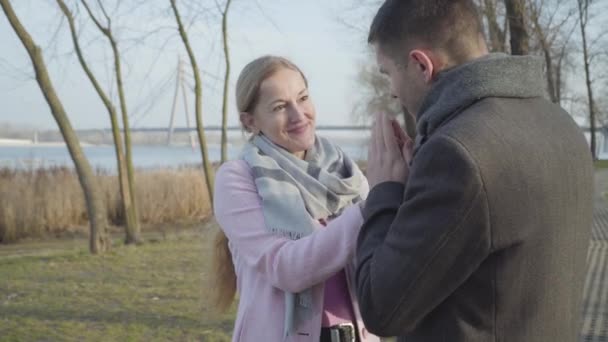 Retrato de mujer caucásica adulta feliz con ojos marrones mirando con amor al hombre calentando sus manos con respiración. Sonriente dama disfrutando de un soleado día de otoño al aire libre con cariño. Amor, ocio, romance — Vídeo de stock