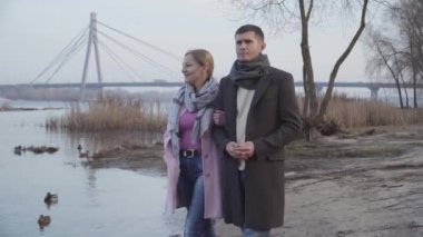 Yaş farkı olan beyaz bir çifti şehir parkında nehir kenarında yürürken mutlu bir şekilde sevin. Olumlu yetişkin erkek ve yaşlı kadının su yüzeyinde yüzen ördeklere hayran portresi. Aşk, flört..