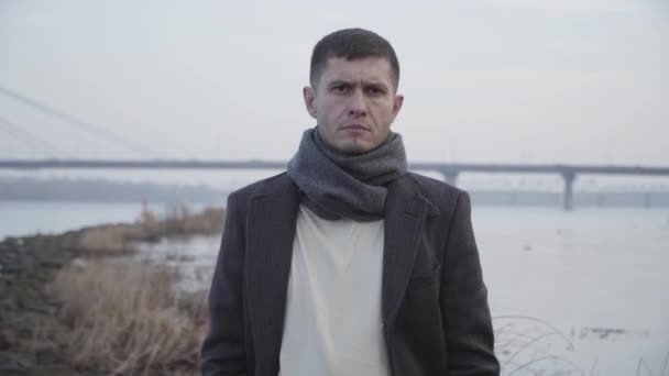 Portrait d'un homme caucasien malheureux posant à l'arrière-plan du pont de la rivière et de la ville. Un jeune homme énervé regardant la caméra et soupirant. Problèmes, stress, dépression . — Video