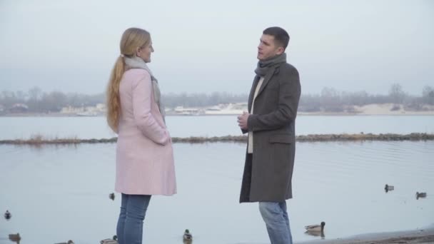 Guapo joven caucásico hombre de pie sobre una rodilla y dando anillo de bodas a la mujer mayor. Elegante novio proponiendo a la señora rubia con estilo en el parque de la ciudad en la orilla del río. Romance, amor, naturaleza, felicidad . — Vídeo de stock