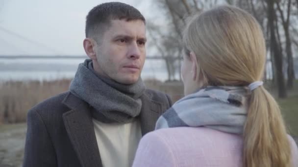 Portrait of confident brunette Caucasian man talking to unrecognizable adult woman outdoors. Serious couple standing head to head in park on autumn day. Love, relationship, support. — Stock Video