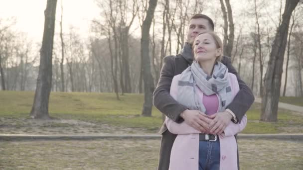 Leende brunett vit man kramar äldre kvinna i parken och pekar bort. Porträtt av lyckliga par med åldersskillnad njuter av helger tillsammans utomhus. Kärlek, avkoppling, livsstil. — Stockvideo