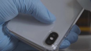 Koruyucu eldivenli, akıllı telefonu peçeteyle ovalayan kadın elinin yakın çekimi. Covid-19 karantinasında telefonu dezenfektanla dezenfekte eden tanınmamış bir kadın. Hijyen, sağlık, koronavirüs..