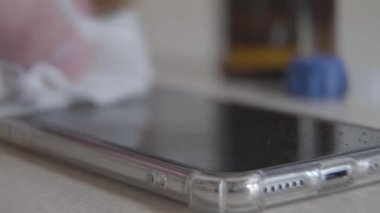 Beyaz dezenfektan peçeteyle telefon ekranını ovuşturan beyaz bir erkek. Dezenfektanla akıllı telefonu silen tanınmayan bir adamın yakın çekimi. Covid-19, hijyen, koronavirüs, karantina.