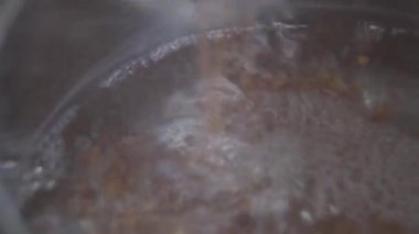 Kaynar suya karabuğday taneleri eklemek. Kahvaltı lapası pişirme sürecine yakın çekim. Mutfak, sağlıklı beslenme, yaşam tarzı..