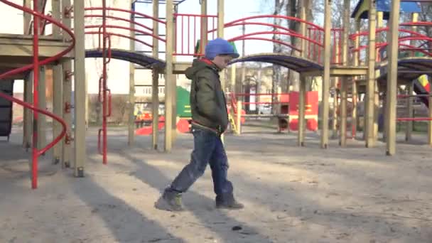 Feldúlt kaukázusi kisfiú, aki egyedül tölti a tavaszi napot a játszótéren. Egy iskolás fiú sétál a szabadban a koronavírus karanténon. Covid-19 világjárvány, életmód, szabadidő. — Stock videók