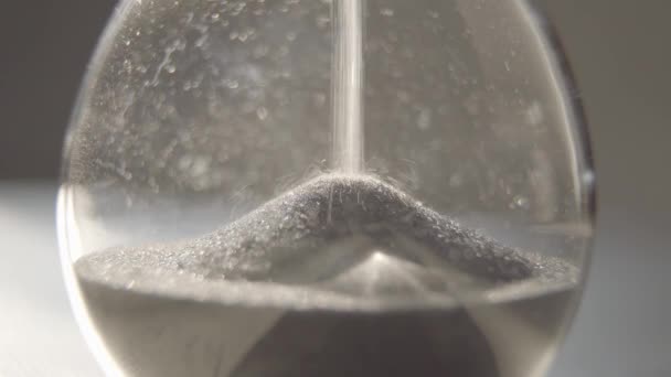 Detailní záběr spodní části přesýpacích hodin s šedým pískem padajícím dolů. Průhledná doba měření pískového skla. Koncepce měření života, sekundy, načasování. — Stock video
