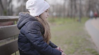 Parkta bankta oturan ve yüzünü buruşturan güzel esmer kızın yan görüntüsü. Güneşli bir günde parkta tek başına dinlenen neşeli bir çocuğun portresi. Yaşam tarzı, rahatlık, rahatlık, yalnızlık..