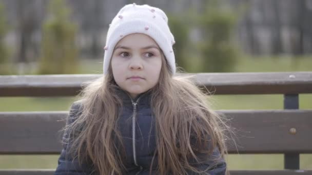 Close-up portret van schattig brunette Kaukasisch meisje met bruine ogen zittend op bank en pratend. Vrolijk kind brengt zonnige lente- of herfstdag buiten door. Vrije tijd, jeugd, levensstijl. — Stockvideo