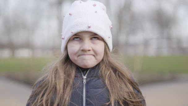 Close-up Gesicht des lustigen kleinen Mädchens macht Gesichter. Porträt eines brünetten kaukasischen Kindes, das an einem sonnigen Frühlingstag im Park grimassiert. Freizeit im Freien, Lifestyle, Spaß. — Stockvideo