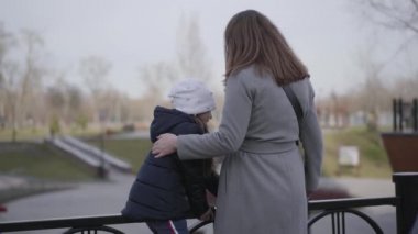 Tanımlanamayan beyaz kadın küçük kızın çitten atlamasına yardım ediyor. Anne ve kızının parkta dinlenme görüntüsü. Birlik, eğlence, yaşam tarzı, çocukluk, annelik.