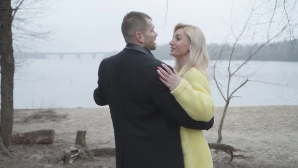 Boldog szerető kaukázusi pár ölelkezik a folyóparton és mosolyog. Vidám, elegáns férfi és nő beszél és néz félre a szabadban. Szerelem, szabadidő, életmód, egység, romantika. — Stock videók