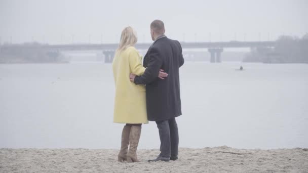 Широкий снимок любящей взрослой пары, стоящей на берегу реки и разговаривающей. Счастливый белый мужчина и женщина встречаются в облачный день на открытом воздухе. Отдых, образ жизни, любовь, романтика . — стоковое видео