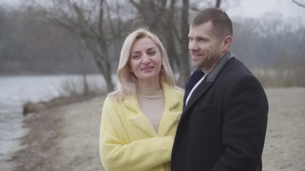 Happy loving blond woman listening to elegant man and smiling. Portrait of joyful adult Caucasian couple dating outdoors on riverbank. Love, romance, lifestyle, leisure. — Stock Video
