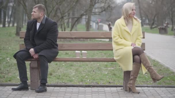 Široký záběr argumentoval, že bělošský pár sedí v parku na opačných stranách lavičky a dívá se jinam. Podrážděný muž a žena mají problémy se vztahem. Životní styl, manželství, konflikt. — Stock video