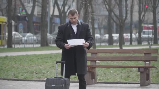 Hombre caucásico insatisfecho plegable mapa y sacudiendo la cabeza como de pie en el callejón en el parque. Retrato de turista masculino disgustado parado en ciudad extranjera con bolsa de viaje. Estilo de vida, viajes, problemas . — Vídeos de Stock