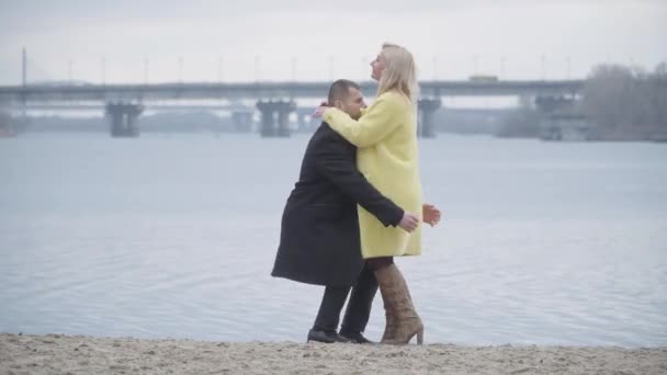 Šťastný kavkazský muž a žena se scházejí na břehu řeky v zamračený den. Milující muž vychovávající blonďatou veselou ženu. Pojem láska, romantika, péče, randění. Životní styl. — Stock video