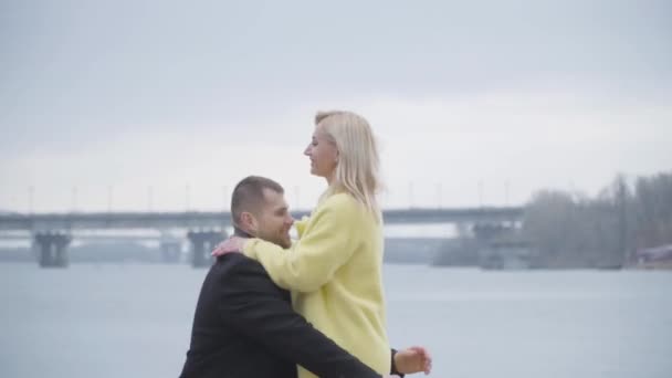 Sonriendo hombre y mujer caucásicos caminando el uno hacia el otro a lo largo de la orilla del río. Vista lateral de marido feliz criando hermosa esposa rubia. Romance, amor eterno, estilo de vida, romance . — Vídeo de stock