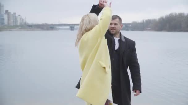 Feliz pareja de adultos bailando y abrazándose en la orilla del río. Retrato de hombre y mujer adultos positivos citas al aire libre. Alegría, estilo de vida, romance, ocio, felicidad . — Vídeo de stock