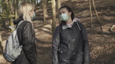 Yüz maskeli ve açık havada konuşan iki kadın arkadaş. Covid-19 'da parkta dinlenen güzel genç kadınların portresi. Yaşam tarzı, milenyum, karantina.