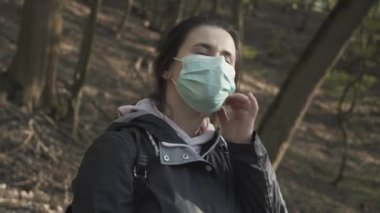Gülümseyen genç bir kadının yüz maskesini çıkardığı ve bahar parkında temiz hava soluduğu yakın plan. Covid-19 tecridinden sonra açık havada güneşli bir gün geçiren Kafkasyalı esmer kız kutlu olsun. Neşe, yaşam tarzı, salgın.