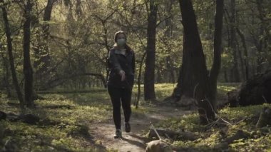 Genç esmer beyaz kadın köpeğiyle güneşli ormanda ya da parkta geziniyor. Neşeli genç kız maskesini çıkarıp evcil hayvanla gidiyor. Doğa, boş zaman, Covid - 19, yaşam tarzı.
