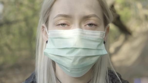 Extrem närbild av ung blond kvinna som tar av ansiktsmask och ler mot kameran. Porträtt av charmig vit flicka med hasselögon som poserar i solljus utomhus. Covid-19, livsstil. — Stockvideo