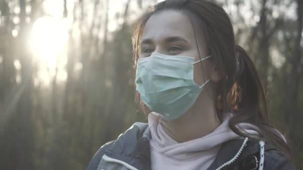 Linda chica morena quitándose la mascarilla y sonriendo. Primer plano de la linda mujer caucásica posando al atardecer en el bosque. Estilo de vida Covid-19, bloqueo del coronavirus, cuarentena pandémica . — Vídeos de Stock