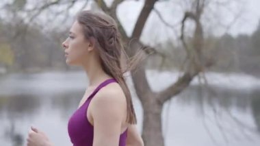 Parkta göl kıyısında koşan kendine güvenen beyaz kadın. İnce esmer kız sabahları dışarıda koşuyor. Fitness, sağlıklı yaşam tarzı, spor, egzersiz.