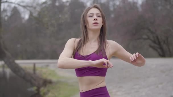 Bella sportiva bruna che si estende all'aperto al mattino. Snella giovane donna in viola abbigliamento sportivo svolta e piegatura sulla riva del lago. Sport, salute, stile di vita, fitness . — Video Stock