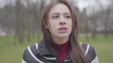 Güzel beyaz bir kızın dış dünyayla konuşup etrafa bakındığı yakın plan bir yüz. Baharda ya da sonbahar parkında güzel bir kadının portresi. Boş zaman, doğa, yaşam tarzı, neşe.