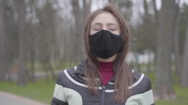 Yüz maskeli, kendine güvenen beyaz bir kadın boş parka bakıyor. Esmer kız Covid-19 karantinası sırasında dışarıda duruyor. Coronavirus salgını, enfeksiyon salgını, yaşam tarzı.