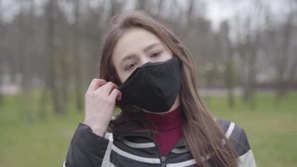 Porträtt av brunett flicka ta av skyddande mask och röra ansiktet. Ung kaukasisk kvinna som ignorerar karantän för coronavirus. Covid-19 pandemi, utbrott av infektionssjukdomar, virusspridning. — Stockvideo