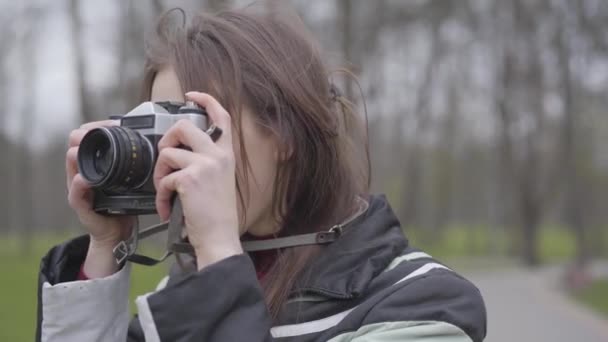 Detailní portrét pozitivní fotografky s kamerou. Mladá vzrušená žena fotí přírodu v parku. Bruneta s hnědýma očima a koníčky venku. Volný čas, životní styl, kreativita. — Stock video