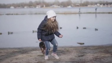 Nehir kıyısında ya da göl kıyısında koşuşturan küçük beyaz bir kız. Güzel ev sahibiyle dışarıda eğlenen neşeli bir evcil hayvan. Eğlence, eğlence, yaşam tarzı, doğa..