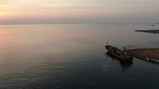 Stary rozbity statek stojący w pomarańczowym słońcu na cypryjskim kurorcie. Spokojne wody Morza Śródziemnego o zachodzie słońca. Spokój, piękno, przyroda, turystyka. Widok drona. — Wideo stockowe