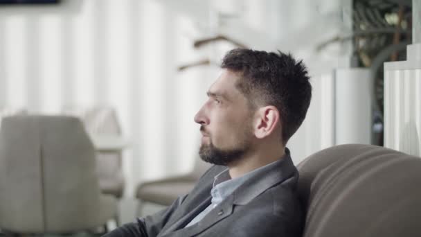 Jeune homme brune portant des écouteurs et se penchant dans le fauteuil. Vue de côté portrait d'un bel homme d'affaires caucasien reposant dans la zone de départ VIP de l'aéroport. Mode de vie, détente, tourisme — Video