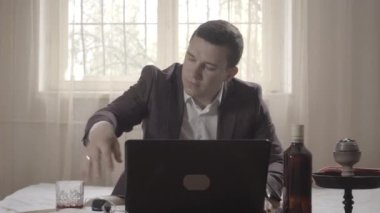 Online video görüşmesini bitiren, alkol içen ve nargile içen Kafkasyalı tatmin olmuş bir adam. Uzaktan çalışma yerine dinlenen rahat çalışan portresi. Covid-19 tecrit yaşam tarzı. S-log-2 ProRes 422 Merkez.