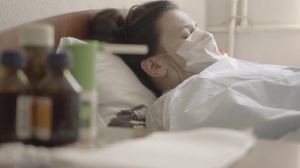 Πλευρική άποψη του άρρωστου καυκάσιου κοριτσιού με μάσκα προσώπου. Κοντινό πλάνο μιας νεαρής μελαχρινής γυναίκας ξαπλωμένης στο κρεβάτι σε νοσοκομείο που πάσχει από νόσο Covid-19. Πανδημία, φάρμακα. S-log-2 ProRes 422 HQ. — Αρχείο Βίντεο