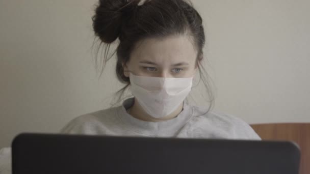 Gros plan portrait de jeune femme malade dans un masque éternuant comme utilisant un ordinateur portable. Brunette fille aux yeux gris travaillant en ligne sur Covid-19 pandémie. Travail à distance, maladie, fatigue. S-log-2 ProRes 422 AC . — Video