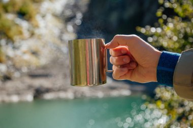 Adam dağlarda bir bardak sıcak içecek tutuyor, arka planda güzel bir göl, Dombay, Kafkasya, Rusya 'da ulusal parkta yürüyüş yapıyor..