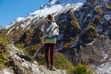 Sırt çantalı genç gezgin kız güneşli bir günde Dombay dağlarında parktaki Rusya 'da yürüyüş yapan Alibek Glasier' in karlı dağlarına bakıyor.