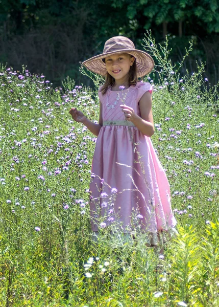 10岁的小女孩穿着漂亮的粉红裙子 头戴软帽 站在鲜花盛开的田野里 微笑着 — 图库照片