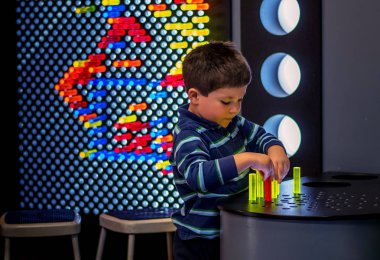 Genç bir çocuk renkli akrilik mandallarla ve ışıklı ızgaralarla oynuyor, renkler ve ışık kullanarak desenler ve şekiller yaratmak için.