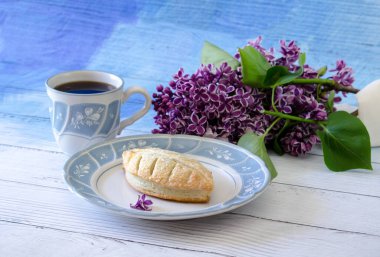 Puf böreği bir fincan sıcak kahve ve güzel bir demet leylak çiçeğiyle servis edilen çikolata reklamı ile doludur.